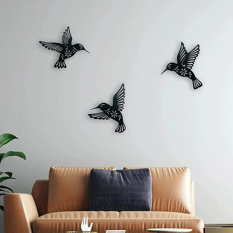 A set of black metal hummingbird wall decor mounted on a light gray wall above a brown sofa.