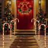 A pathway lined with glowing orange candy cane lights leads to a red door decorated with a Christmas wreath.