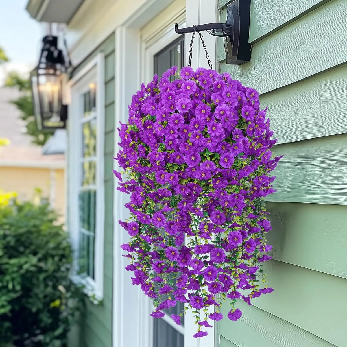 A vibrant purple artificial morning glory hanging vine cascading down a light green siding wall.