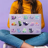 A hand holds a laptop displaying various aesthetic PVC starry sky cat stickers for scrapbooking
