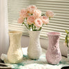 Three white and pink ceramic vases with floral relief designs displayed on a white cloth.