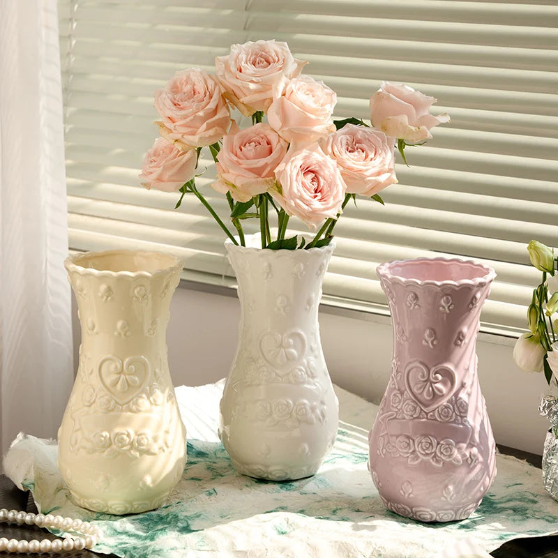 Three white and pink ceramic vases with floral relief designs displayed on a white cloth.