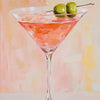 A pink cocktail in a martini glass garnished with two green olives, set against a light background.