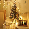 A decorated Christmas tree adorned with warm string lights sits on a white tablecloth.