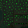 A dark room decorated with green glow-in-the-dark star decals on a wall and a wooden shelf.