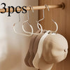Three metal hat storage hooks hanging on a wooden rod, with several beige hats displayed below.
