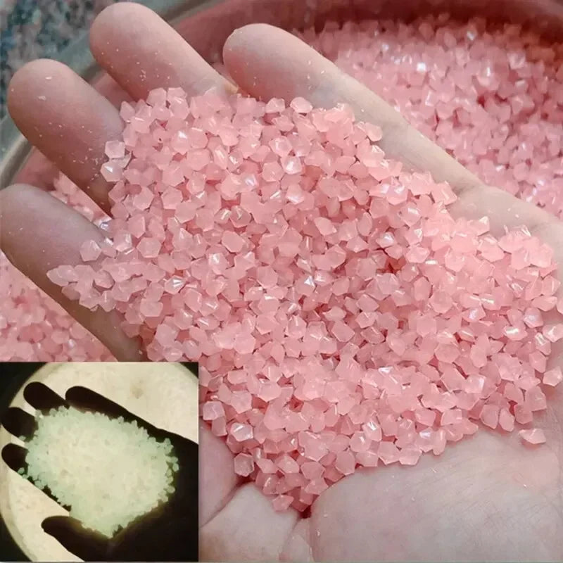 A hand holds a pile of pink glow-in-the-dark luminous pebbles for garden and aquarium decor.