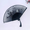 A black vintage bamboo folding fan with sheer fabric and floral decorations shown against a white background.