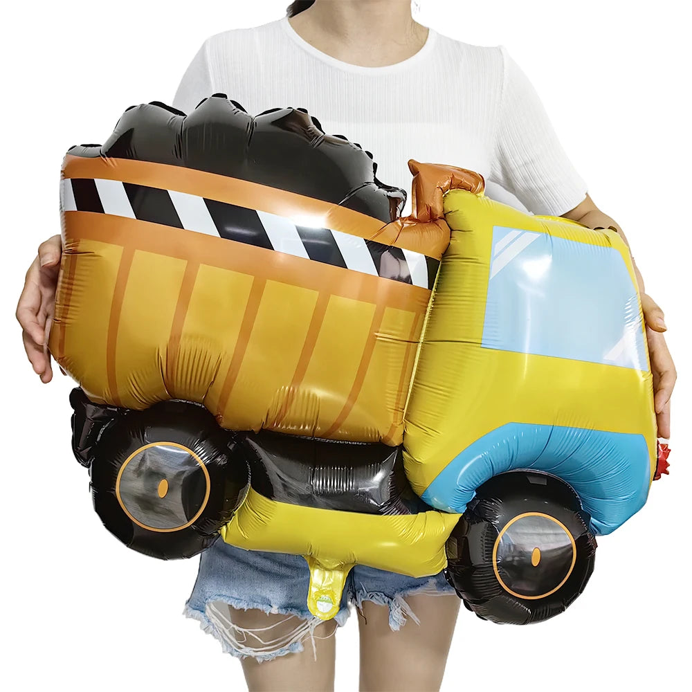A large construction truck shaped foil balloon in yellow and black stripes, held by a person.