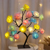 Schwarzer Baum mit leuchtenden gelben, rosa und blauen Rosenblüten als Nachtlicht-Dekoration.