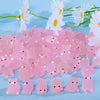 A pile of pink glow-in-the-dark mini pig figurines scattered on a light blue background with white flowers.