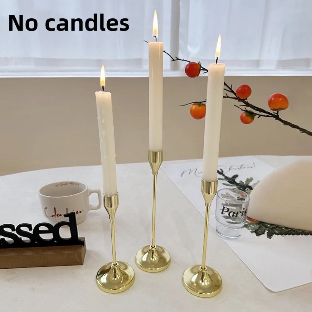 Three gold-toned candle holders with white taper candles and a black sign on a white table.