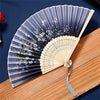 A vintage silk folding hand fan with blue and white floral patterns is displayed on a wooden surface.