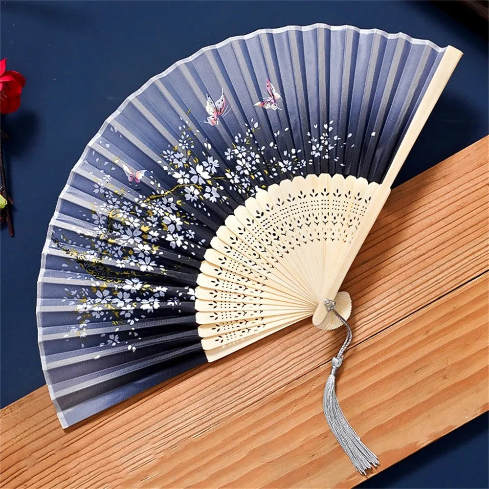 A vintage silk folding hand fan with blue and white floral patterns is displayed on a wooden surface.