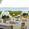 A table setting featuring white flowers and greenery for an outdoor event.