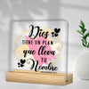 A clear acrylic sign featuring the phrase Dios tiene un plan que lleva tu nombre in black script on a light background.