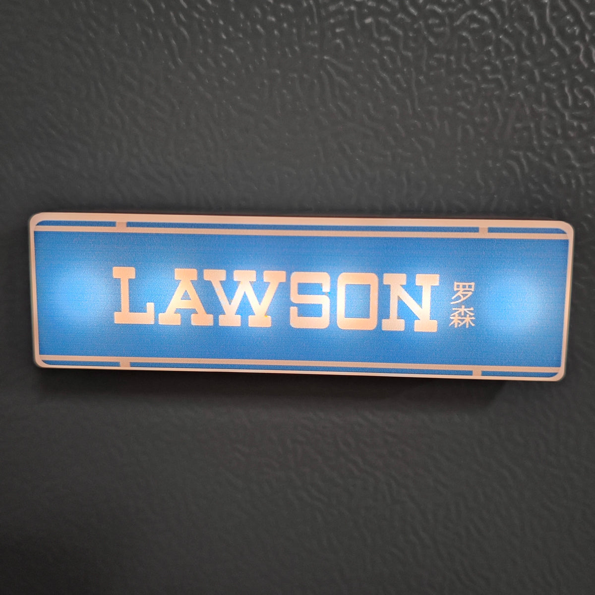 A rectangular blue LED sign with the word LAWSON in gold lettering and Japanese characters on a dark surface.