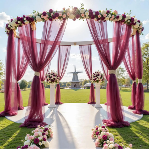 Un elegante telón de boda al aire libre con un arco floral rosa y drapeado de tul transparente.