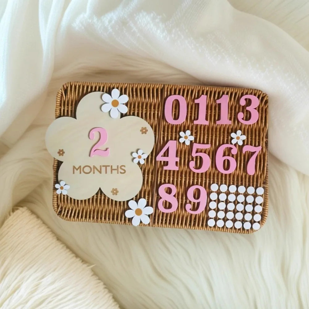 A wooden monthly milestone card featuring the number 2 months and various numbers, set against a white fluffy background.