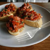 A plate of bruschetta topped with diced tomatoes and herbs, served with a clear plastic fork.
