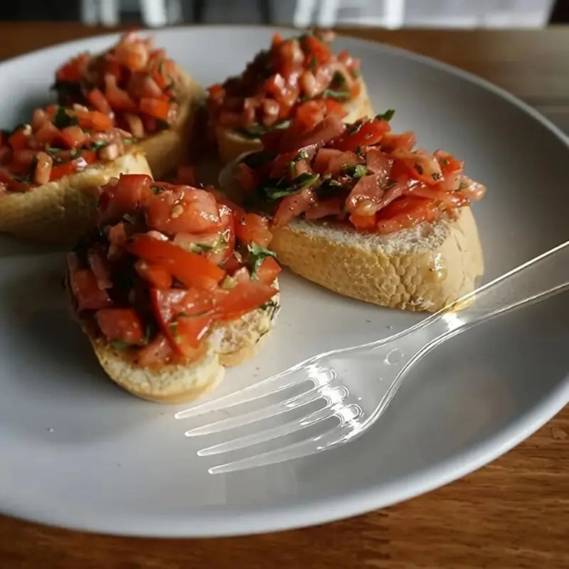 A plate of bruschetta topped with diced tomatoes and herbs, served with a clear plastic fork.