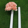 A pink foam flower arrangement is displayed in a white cylinder against a green turf background.