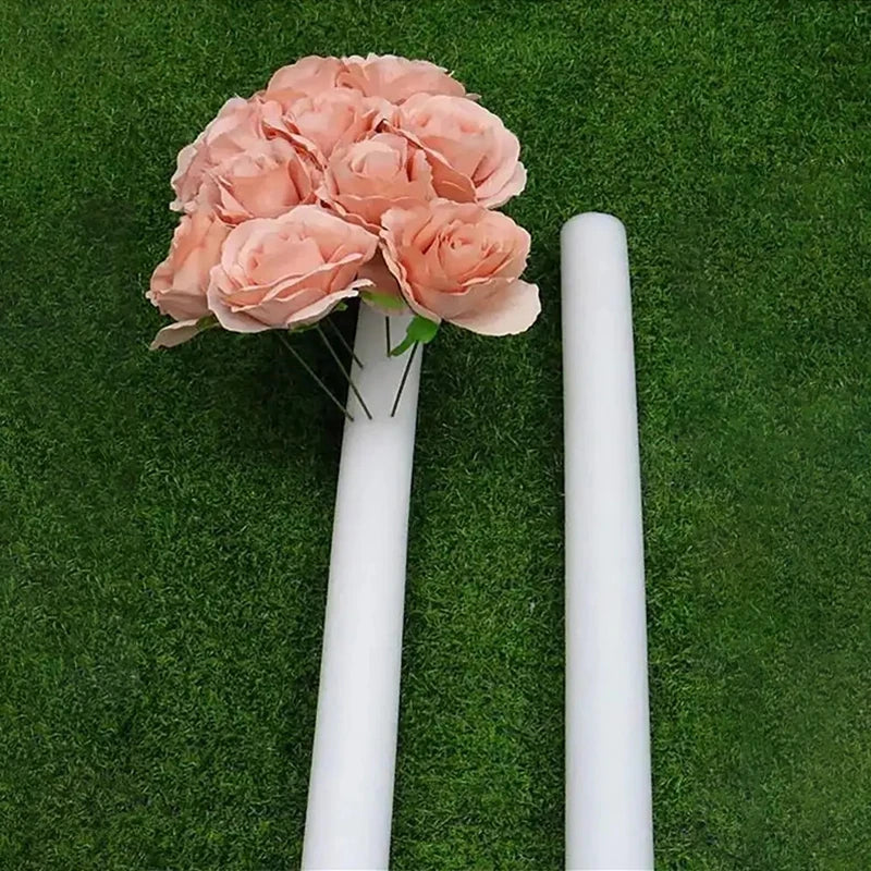 A pink foam flower arrangement is displayed in a white cylinder against a green turf background.
