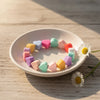 A circular arrangement of colorful silicone heart beads on a white plate, set against a light wooden background.