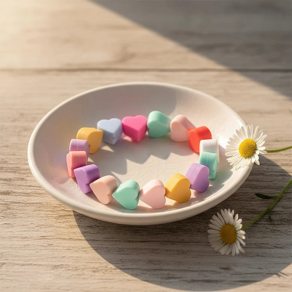 A circular arrangement of colorful silicone heart beads on a white plate, set against a light wooden background.