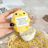 Handmade yellow crochet chicken doll with an inspirational slogan tag and a pocket, resting on a yellow mesh surface.