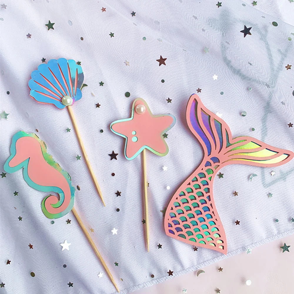 A set of colorful starfish and seashell-shaped wooden party decorations on a white cloth with scattered glitter stars.
