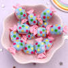 A pink dish holds colorful blue and pink resin cabochons with glitter dots for crafting projects.