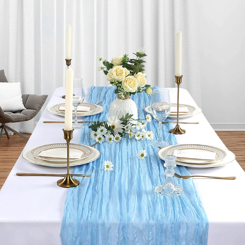 Light blue cheesecloth table runner with white flowers and candles on a white tablecloth for rustic events