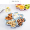 A heart-shaped four-compartment snack tray filled with various dried fruits, nuts, and candies, alongside a glass of juice.