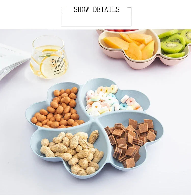 A heart-shaped four-compartment snack tray filled with various dried fruits, nuts, and candies, alongside a glass of juice.