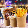 A close-up of several disposable kraft paper cups filled with french fries and toppings, set against a blurred city night bac
