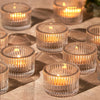 A collection of clear glass tealight candle holders arranged on a textured fabric surface.