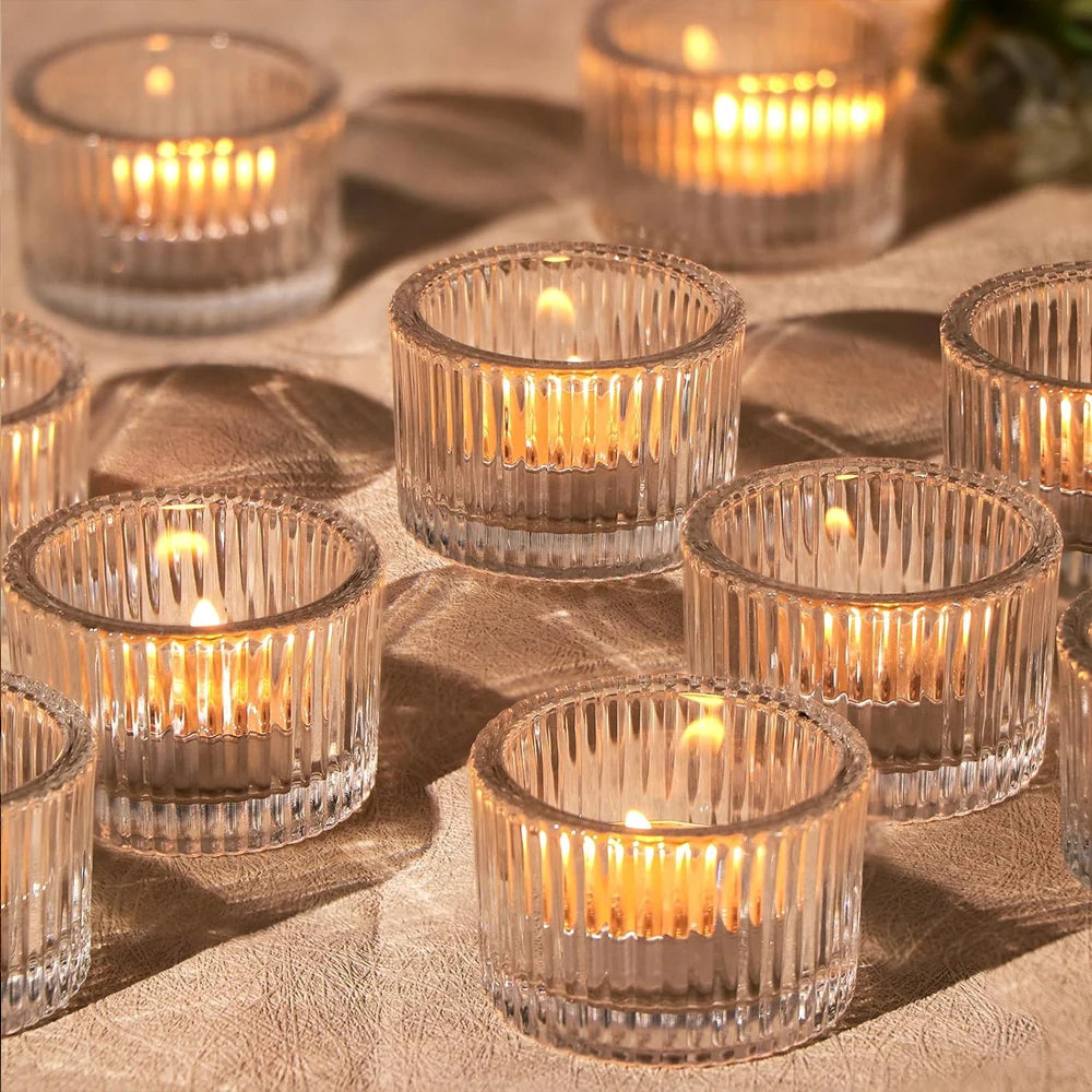 A collection of clear glass tealight candle holders arranged on a textured fabric surface.