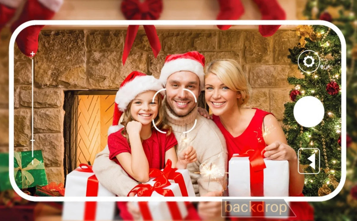 A family of three smiling in front of a rustic stone fireplace with Christmas decorations and gifts.