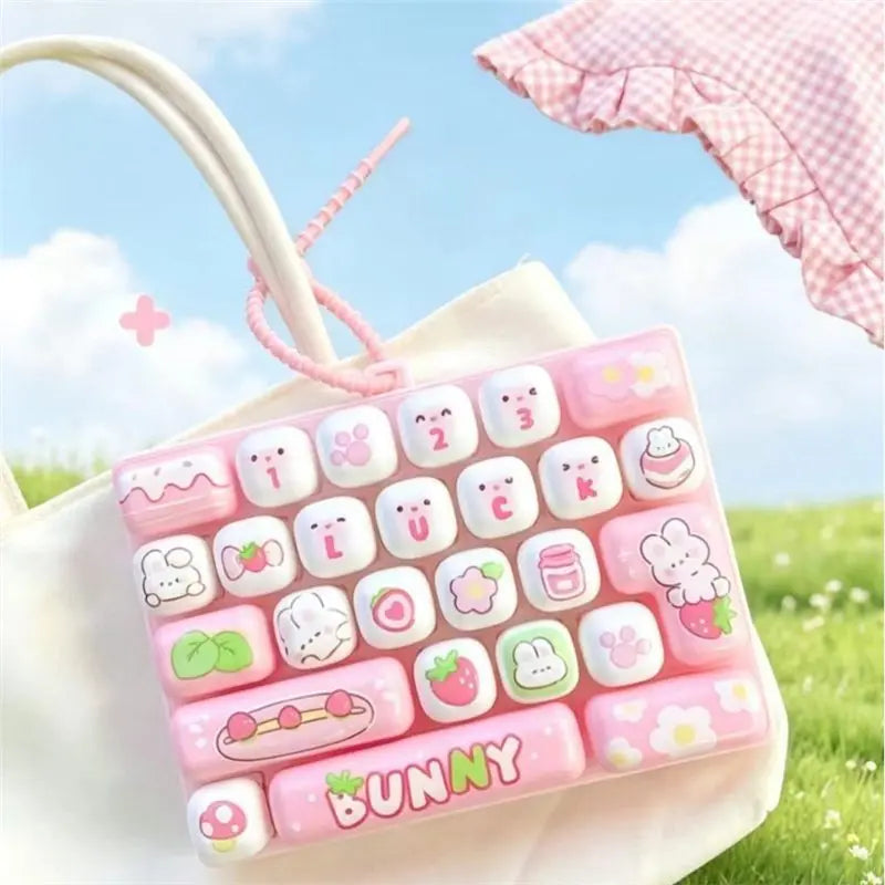 A pink and white cartoon animal keyboard keycap fidget toy is shown attached to a white bag in an outdoor setting.