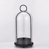 A clear glass dome candle holder with a black base and a metal loop top.
