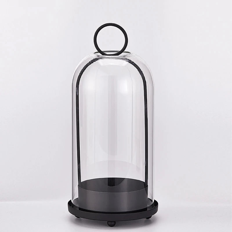 A clear glass dome candle holder with a black base and a metal loop top.