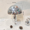 A silver, mushroom-shaped disco ball decoration with a textured surface sits on a white surface.