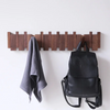 A dark wood wall coat rack with eight hooks displaying a gray towel and a black leather backpack.