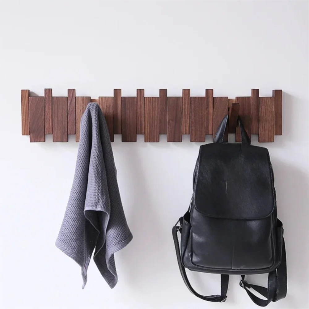 A dark wood wall coat rack with eight hooks displaying a gray towel and a black leather backpack.