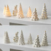 A collection of ceramic glow-in-the-dark mini Christmas tree decor in white and gold on a white shelf.