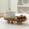 A white ceramic bowl filled with light-colored substance rests on a wooden storage tray with several nuts.