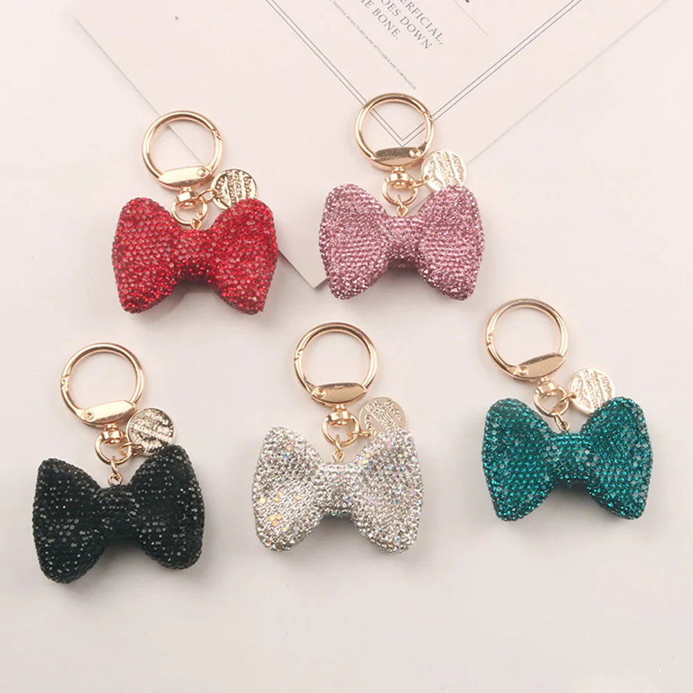 Four sparkling rhinestone bow keychains in red, pink, black, and teal.