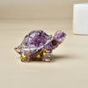 Transparente violette Kristall-Schildkrötenfigur auf einer hellen Oberfläche.