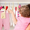 A young child is looking at a rack of baby clothes hanging on hangers with rainbow cloud-shaped dividers.